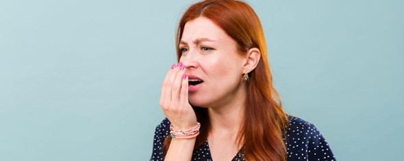 Mujer preocupada por su aliento, tapándose la boca con la mano